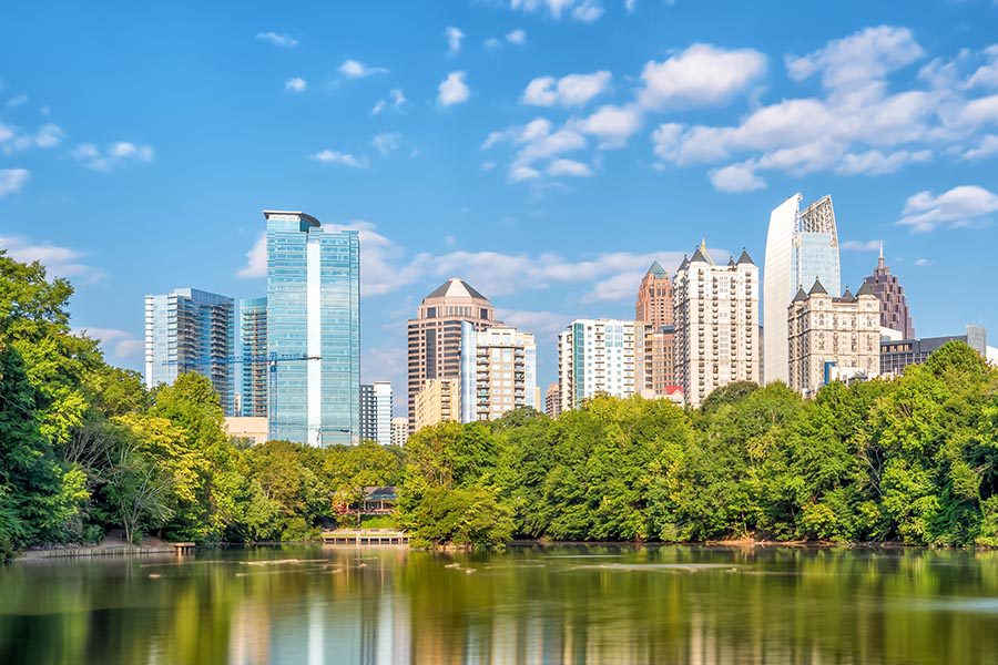 Contact - Distance View of Atlant, GA With a Lake and Trees in Front of Tall Buildings on a Sunny Day