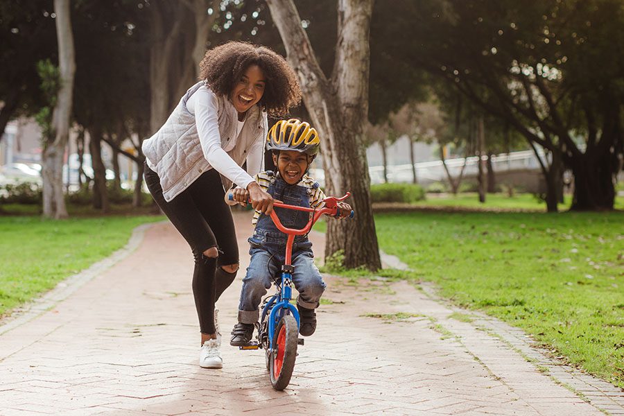 About Our Agency - A Mother is Teaching Her Son to Ride a Bike at a Park