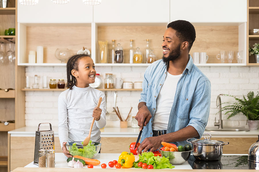 Personal Insurance - A Father and Daughter are Smiling at Each Out While Preparing some Salad in the Kitchen